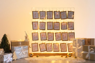 Photo of Handmade advent calendar, gifts and decor on table near light wall. Christmas tradition