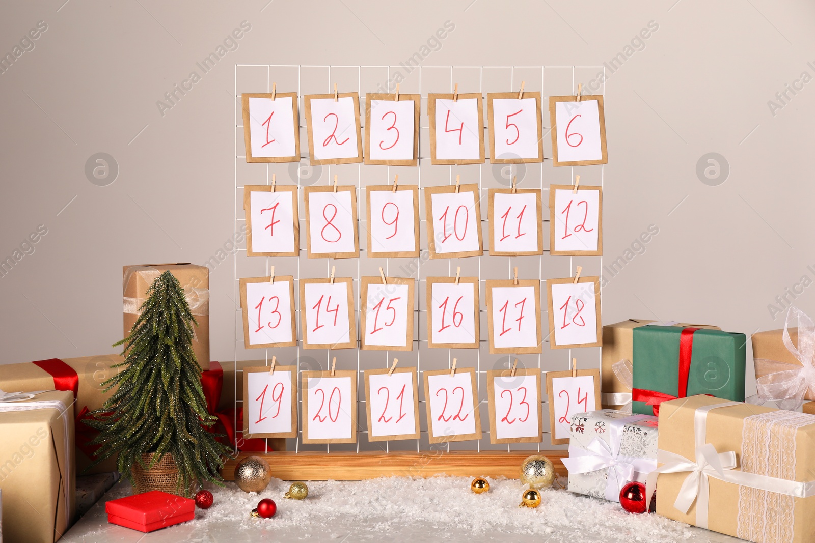 Photo of Handmade advent calendar, gifts and decor on table near light wall. Christmas tradition