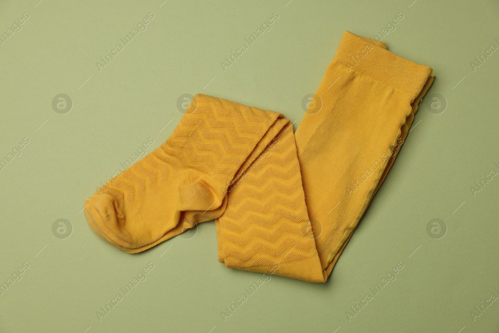 Photo of Beautiful yellow child's tights on green background, top view