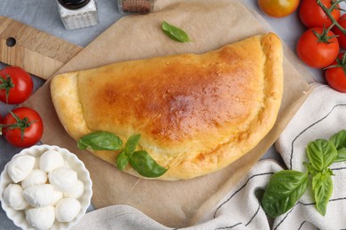 Photo of Tasty vegetarian calzone with tomatoes, mozzarella cheese and basil on grey table, top view