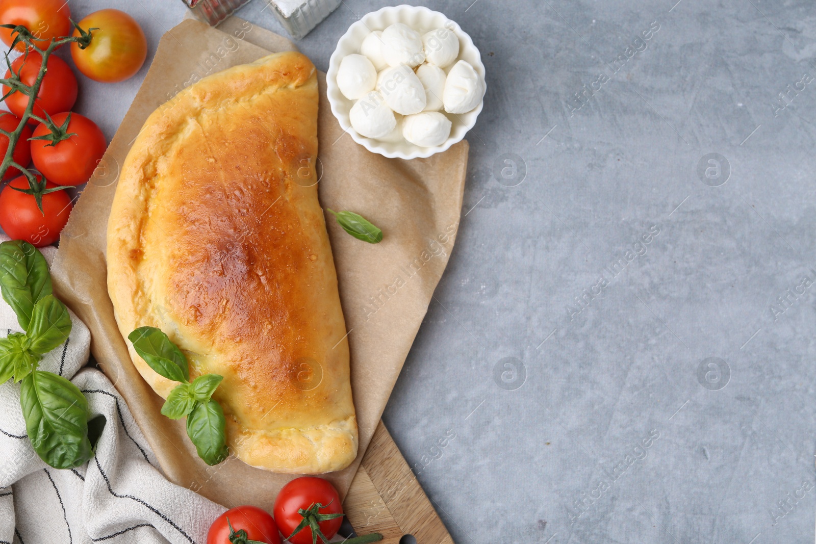 Photo of Tasty vegetarian calzone with tomatoes, mozzarella cheese and basil on grey table, top view. Space for text