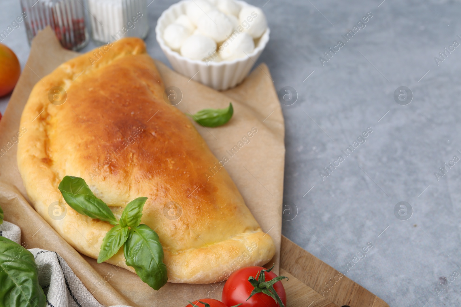 Photo of Tasty vegetarian calzone with basil, mozzarella cheese and tomato on grey table, closeup. Space for text