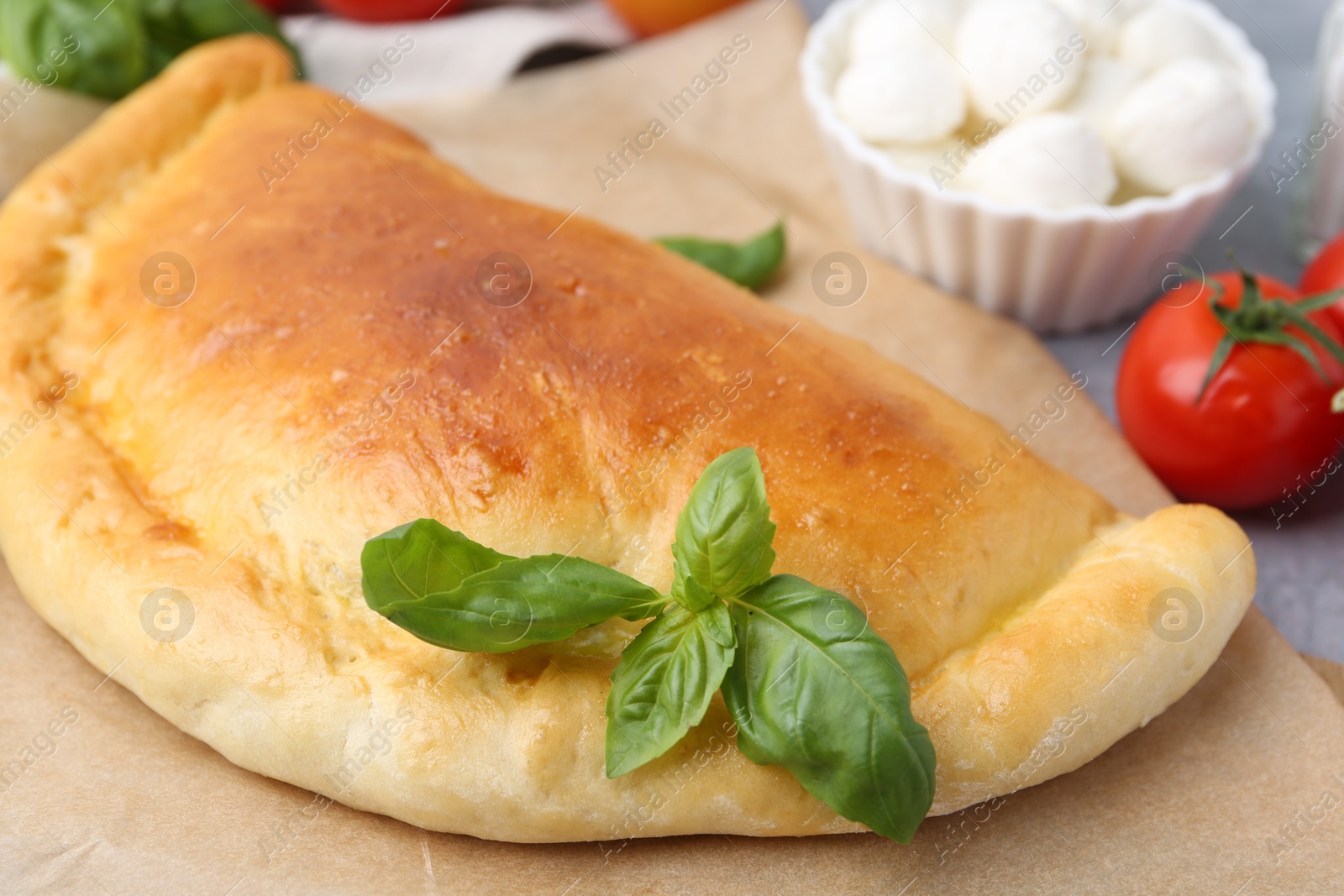 Photo of Tasty vegetarian calzone with basil, mozzarella cheese and tomato on table, closeup