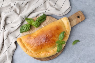 Photo of Tasty vegetarian calzone with basil on grey table, top view