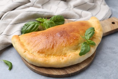 Photo of Tasty vegetarian calzone with basil on grey table, closeup