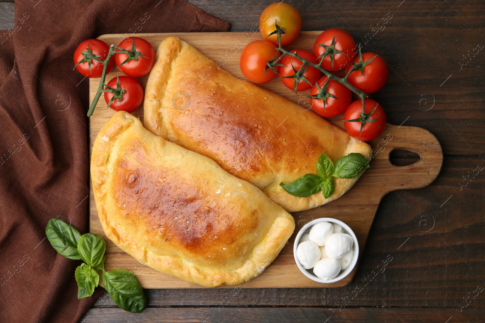 Photo of Tasty vegetarian calzones with basil, mozzarella cheese and tomatoes on wooden table, top view