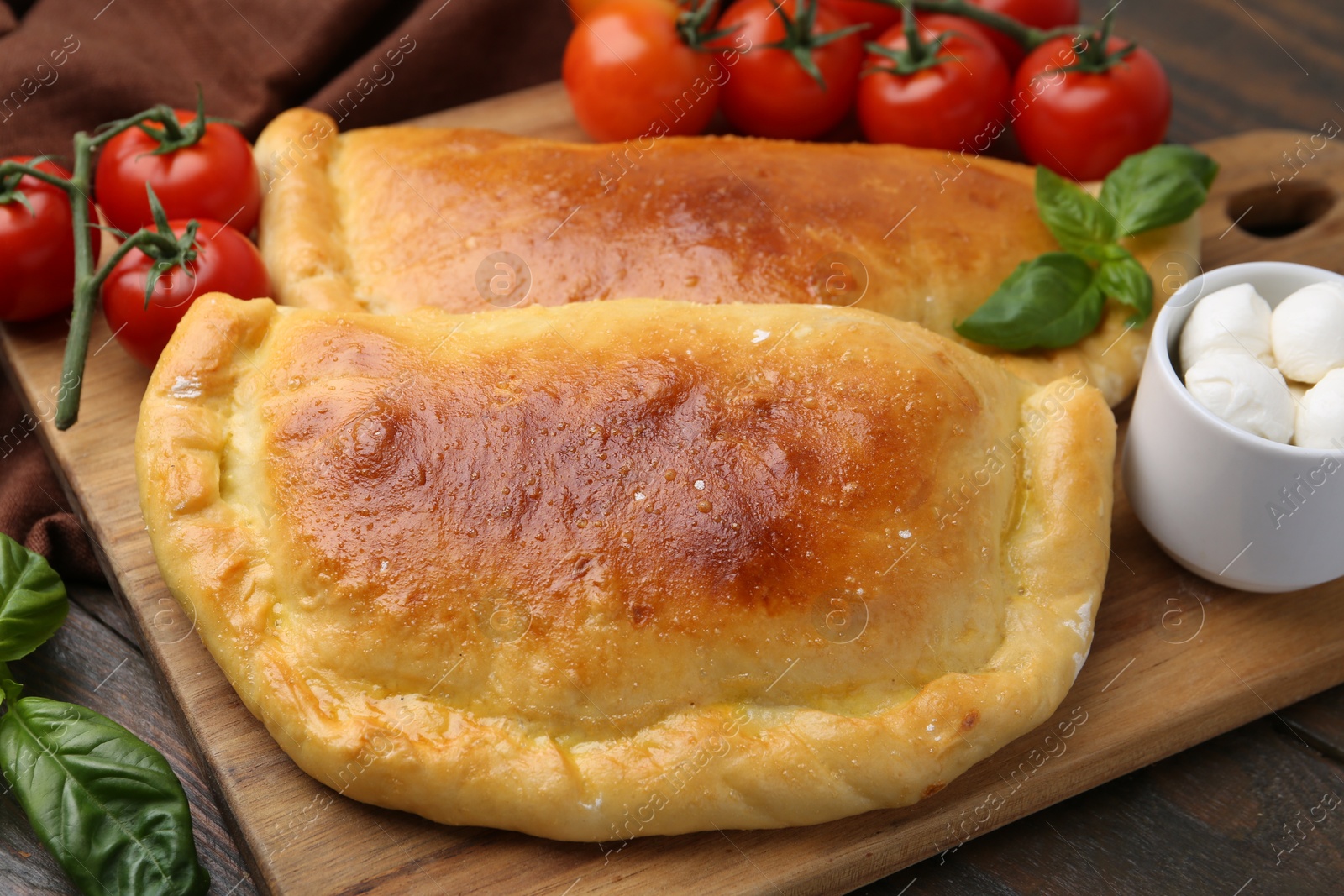 Photo of Tasty vegetarian calzones with basil, mozzarella cheese and tomatoes on wooden table, closeup