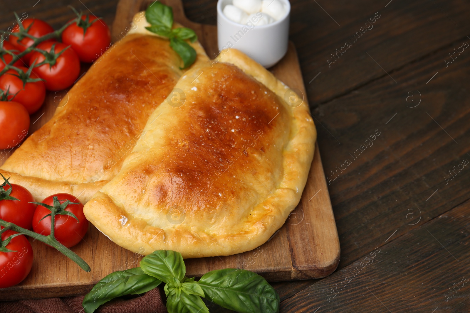 Photo of Tasty vegetarian calzones with basil, mozzarella cheese and tomatoes on wooden table, closeup. Space for text