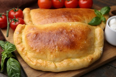 Photo of Tasty vegetarian calzones with basil and tomatoes on wooden table, closeup