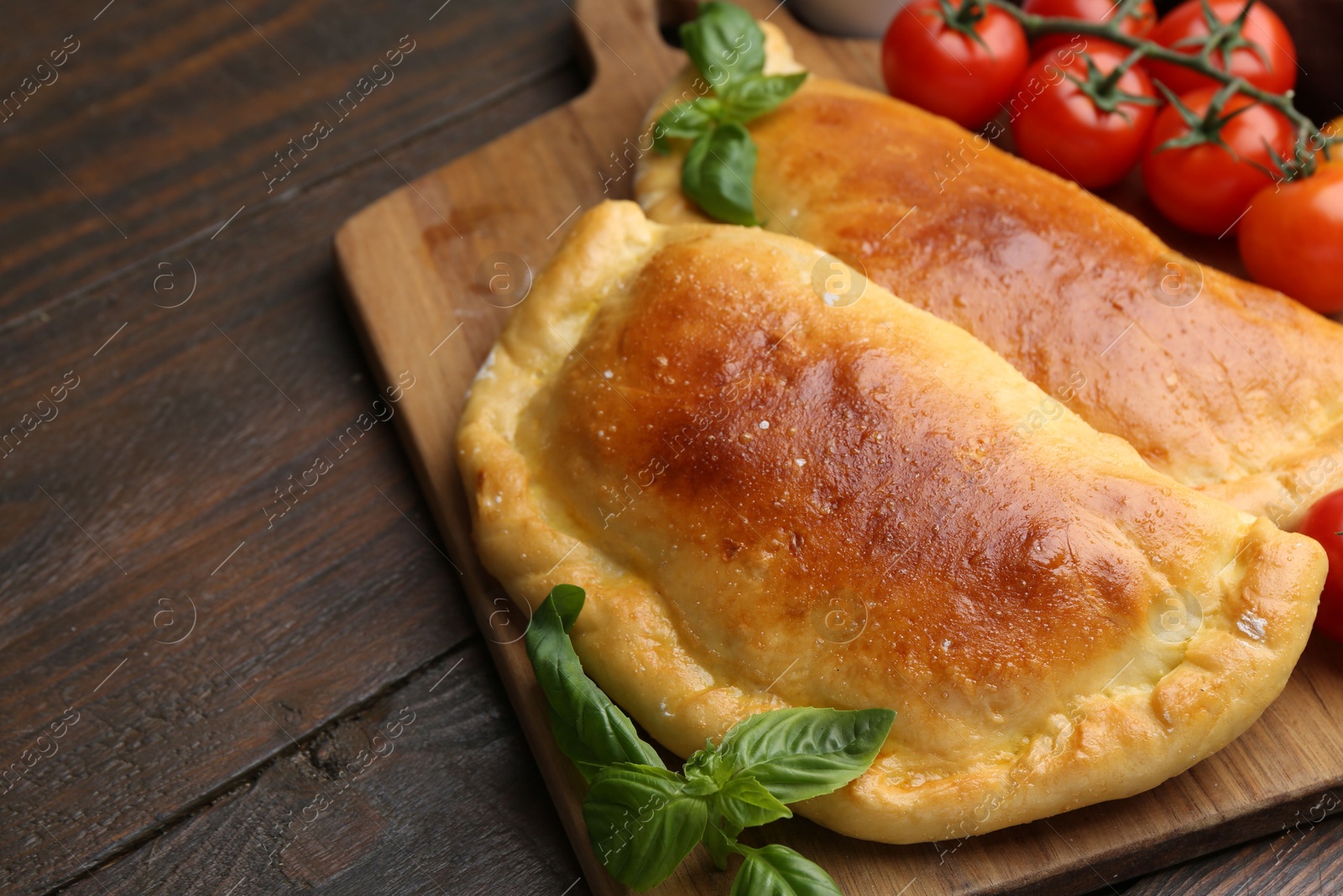 Photo of Tasty vegetarian calzones with basil and tomatoes on wooden table, closeup. Space for text