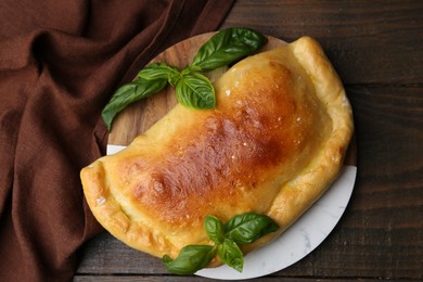 Photo of Tasty vegetarian calzone with basil on wooden table, top view