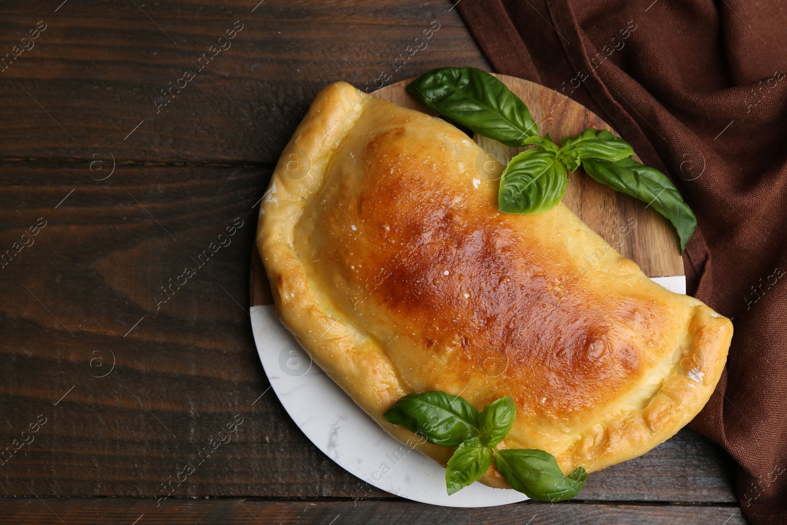 Photo of Tasty vegetarian calzone with basil on wooden table, top view. Space for text