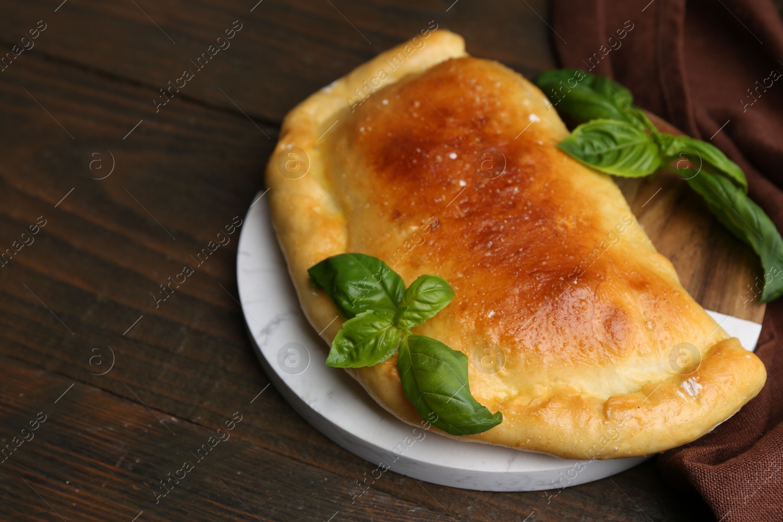 Photo of Tasty vegetarian calzone with basil on wooden table, closeup. Space for text