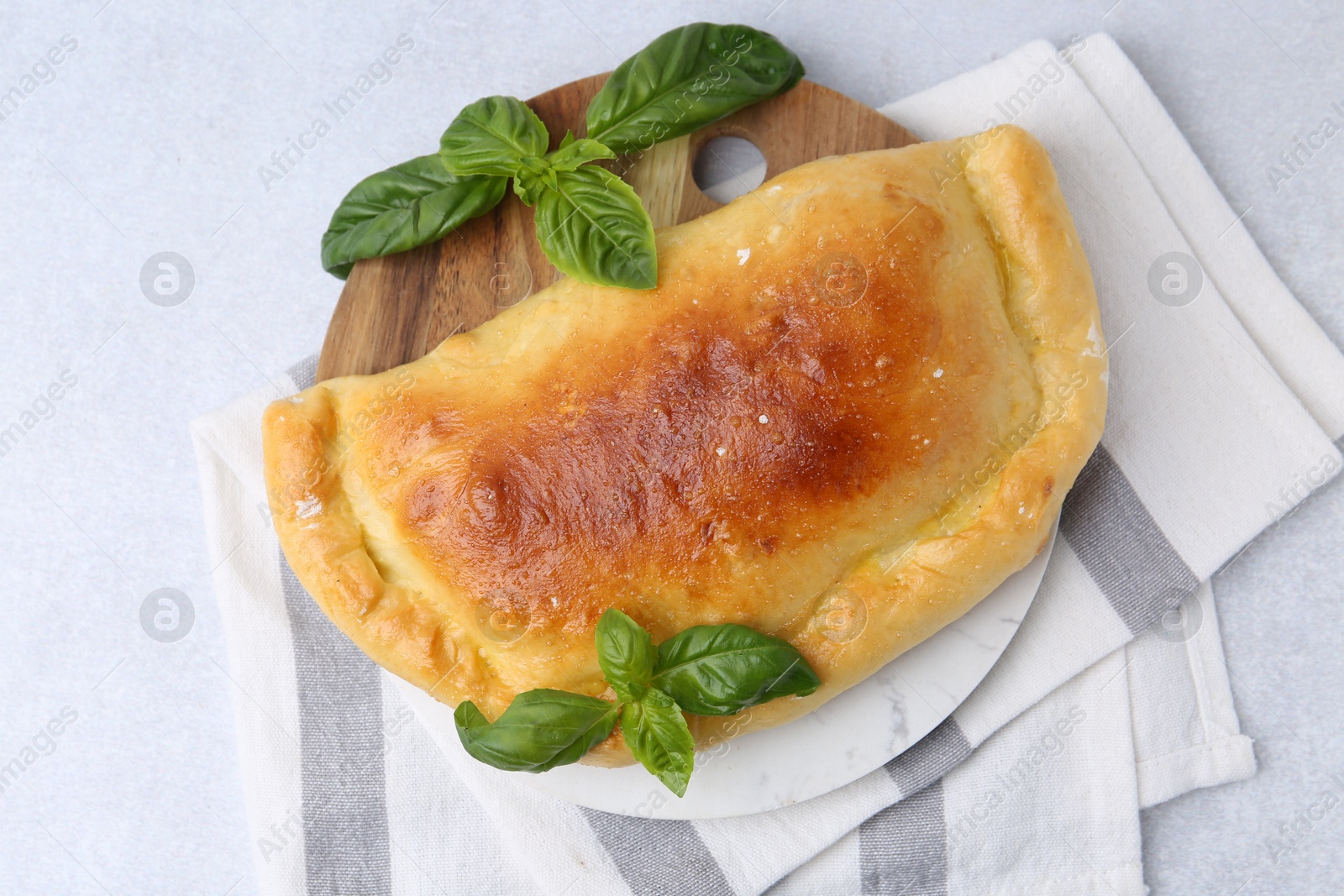 Photo of Tasty vegetarian calzone with basil on light table, top view