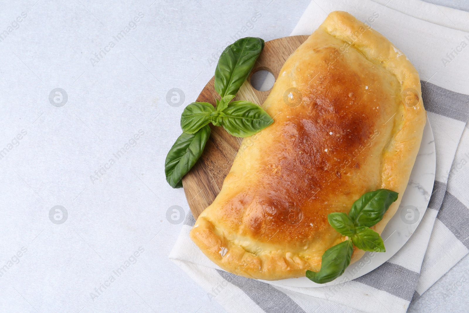 Photo of Tasty vegetarian calzone with basil on light table, top view. Space for text