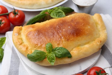 Photo of Tasty vegetarian calzone with basil and tomatoes on table, closeup