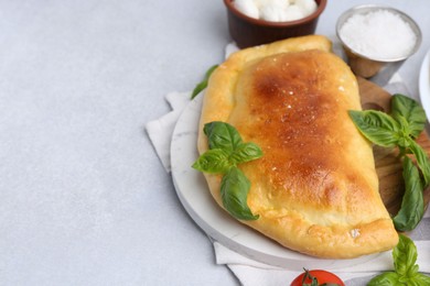 Photo of Tasty vegetarian calzone with basil and mozzarella cheese on light table, closeup. Space for text