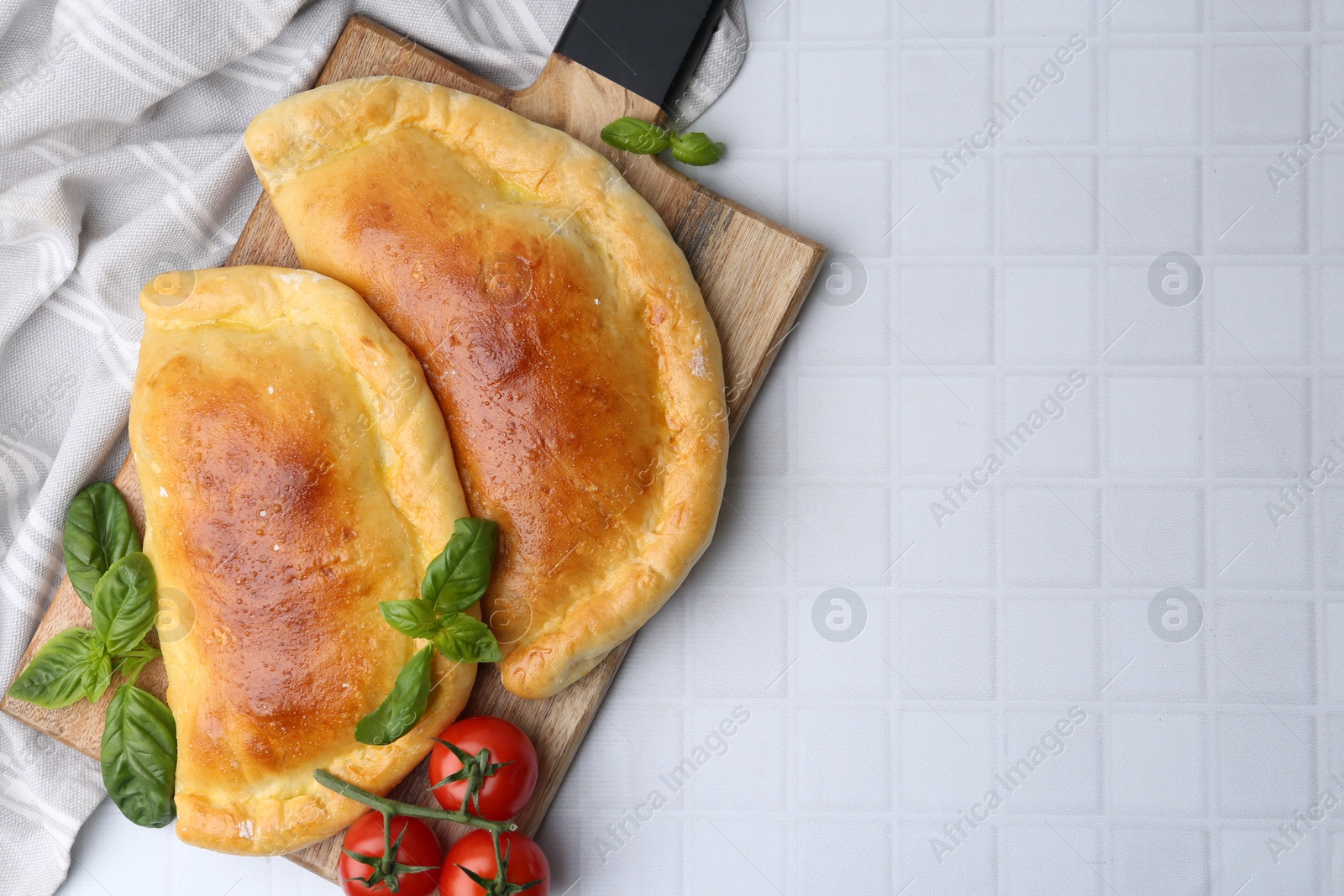 Photo of Tasty vegetarian calzones with basil and tomatoes on white tiled table, top view. Space for text