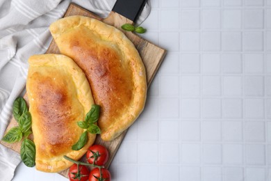 Photo of Tasty vegetarian calzones with basil and tomatoes on white tiled table, top view. Space for text