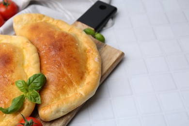 Photo of Tasty vegetarian calzones with basil on white tiled table, closeup. Space for text