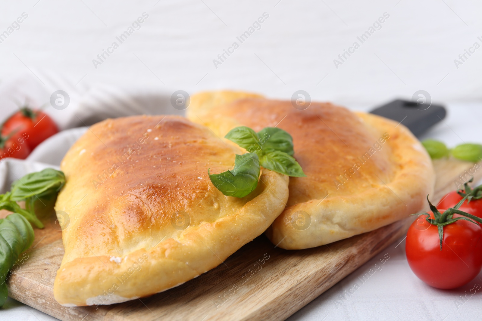 Photo of Tasty vegetarian calzones with basil and tomatoes on white table, closeup