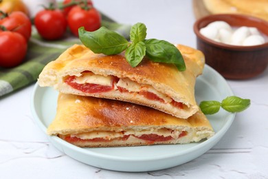 Photo of Pieces of tasty vegetarian calzone with tomato, cheese and basil on white textured table, closeup