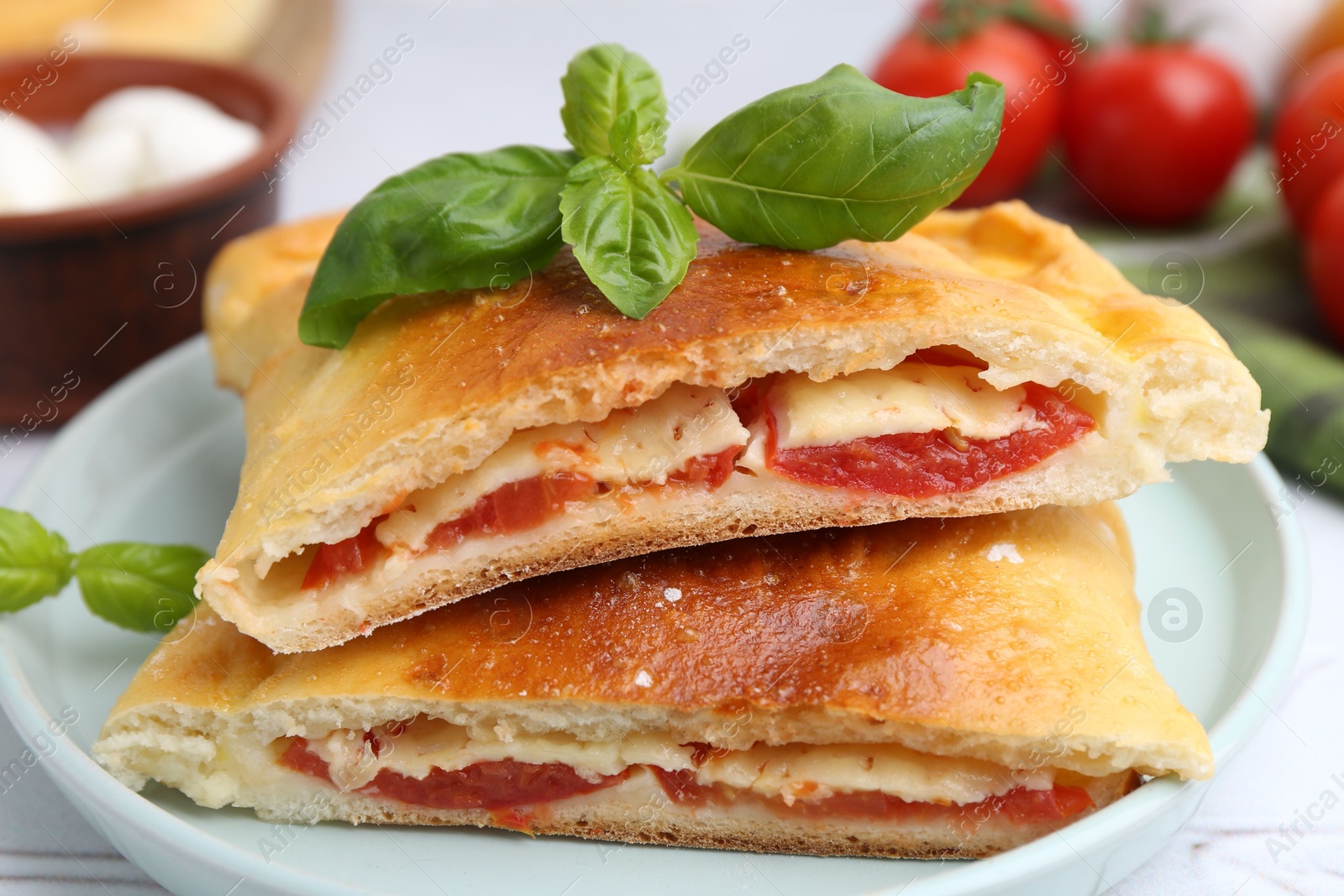 Photo of Pieces of tasty vegetarian calzone with tomato, cheese and basil on table, closeup