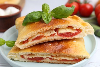 Photo of Pieces of tasty vegetarian calzone with tomato, cheese and basil on table, closeup