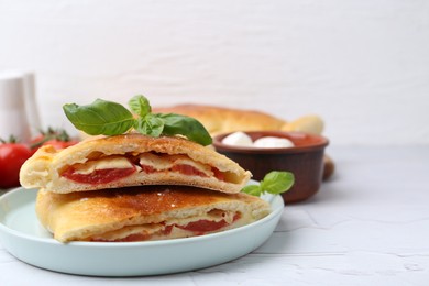 Photo of Pieces of tasty vegetarian calzone with tomato, cheese and basil on white textured table, closeup