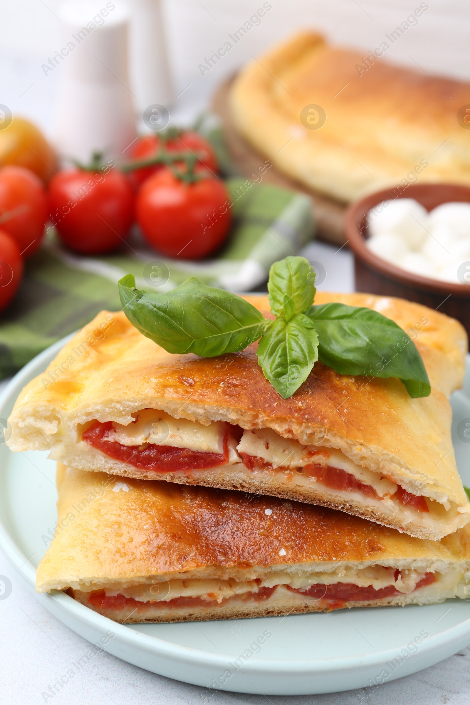 Photo of Pieces of tasty vegetarian calzone with tomato, cheese and basil on table, closeup