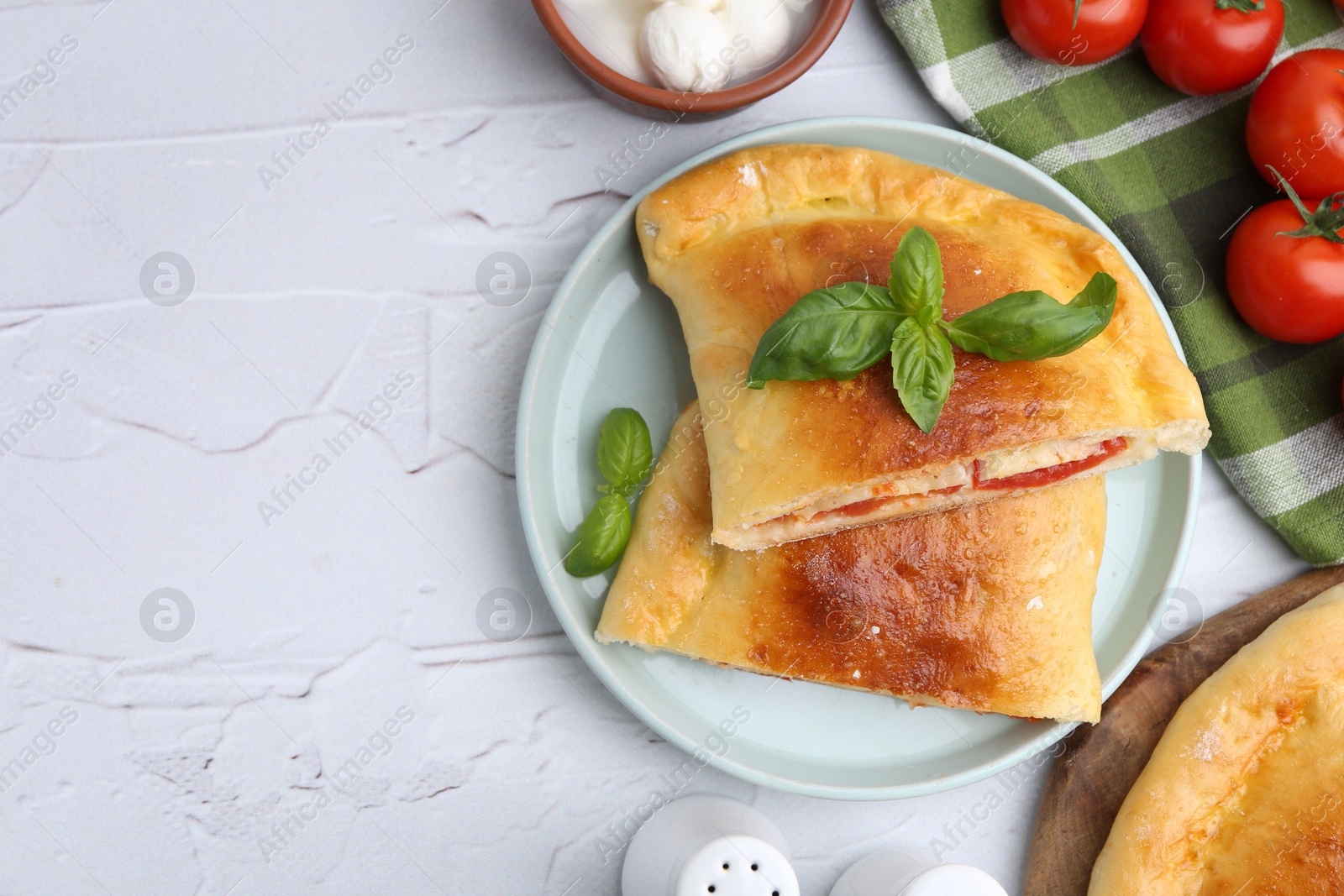 Photo of Pieces of tasty vegetarian calzone with tomatoes, mozzarella cheese and basil on white textured table, top view. Space for text