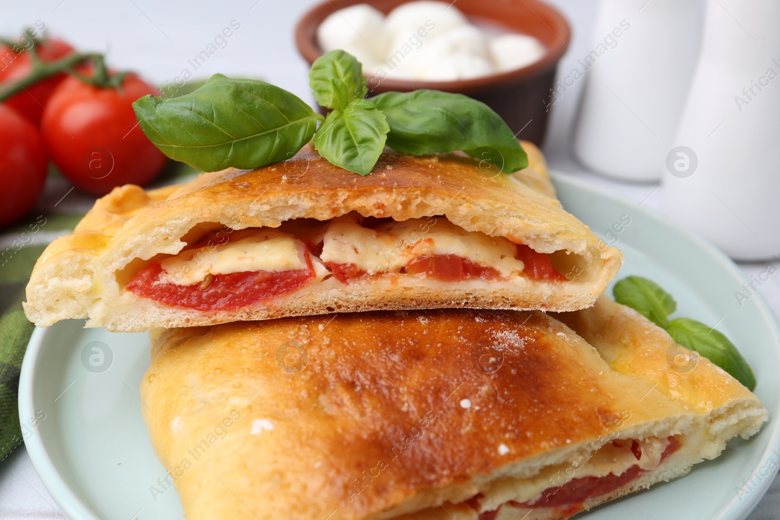 Photo of Pieces of tasty vegetarian calzone with tomato, cheese and basil on table, closeup