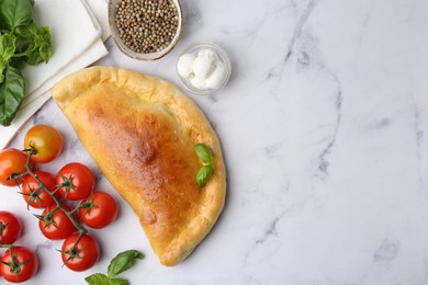 Photo of Tasty vegetarian calzone with tomatoes, mozzarella cheese and spices on white marble table, flat lay. Space for text