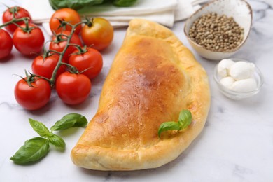 Photo of Tasty vegetarian calzone with tomatoes, mozzarella cheese and spices on white marble table, closeup