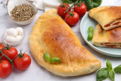 Photo of Tasty vegetarian calzones with tomatoes, mozzarella cheese and spices on white marble table, closeup