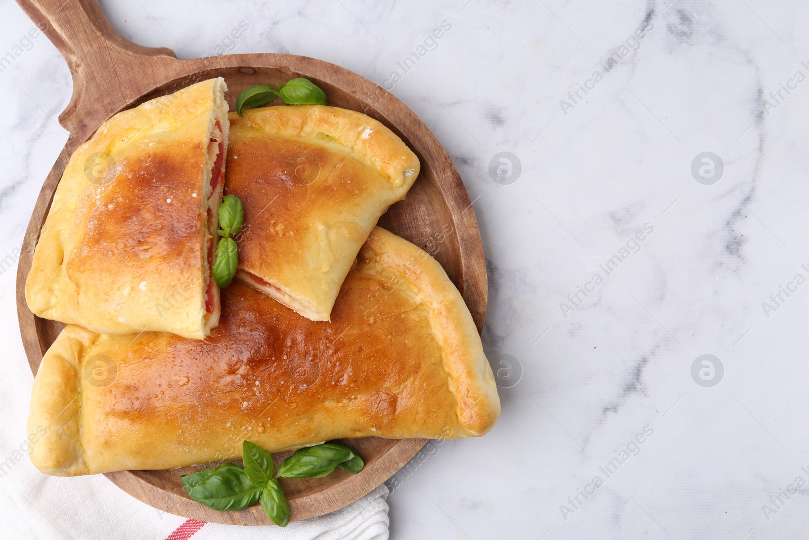 Photo of Tasty vegetarian calzones with tomato, cheese and basil on white marble table, top view. Space for text