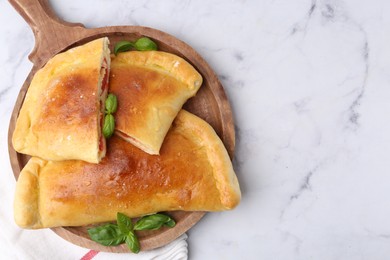 Photo of Tasty vegetarian calzones with tomato, cheese and basil on white marble table, top view. Space for text