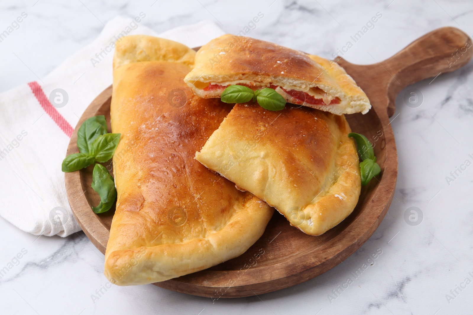 Photo of Tasty vegetarian calzones with tomato, cheese and basil on white marble table, closeup