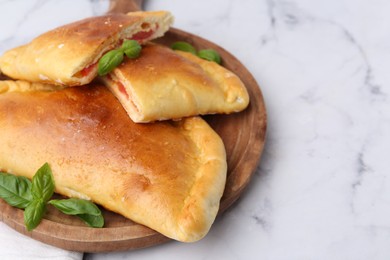 Photo of Tasty vegetarian calzones with tomato, cheese and basil on white marble table, closeup. Space for text