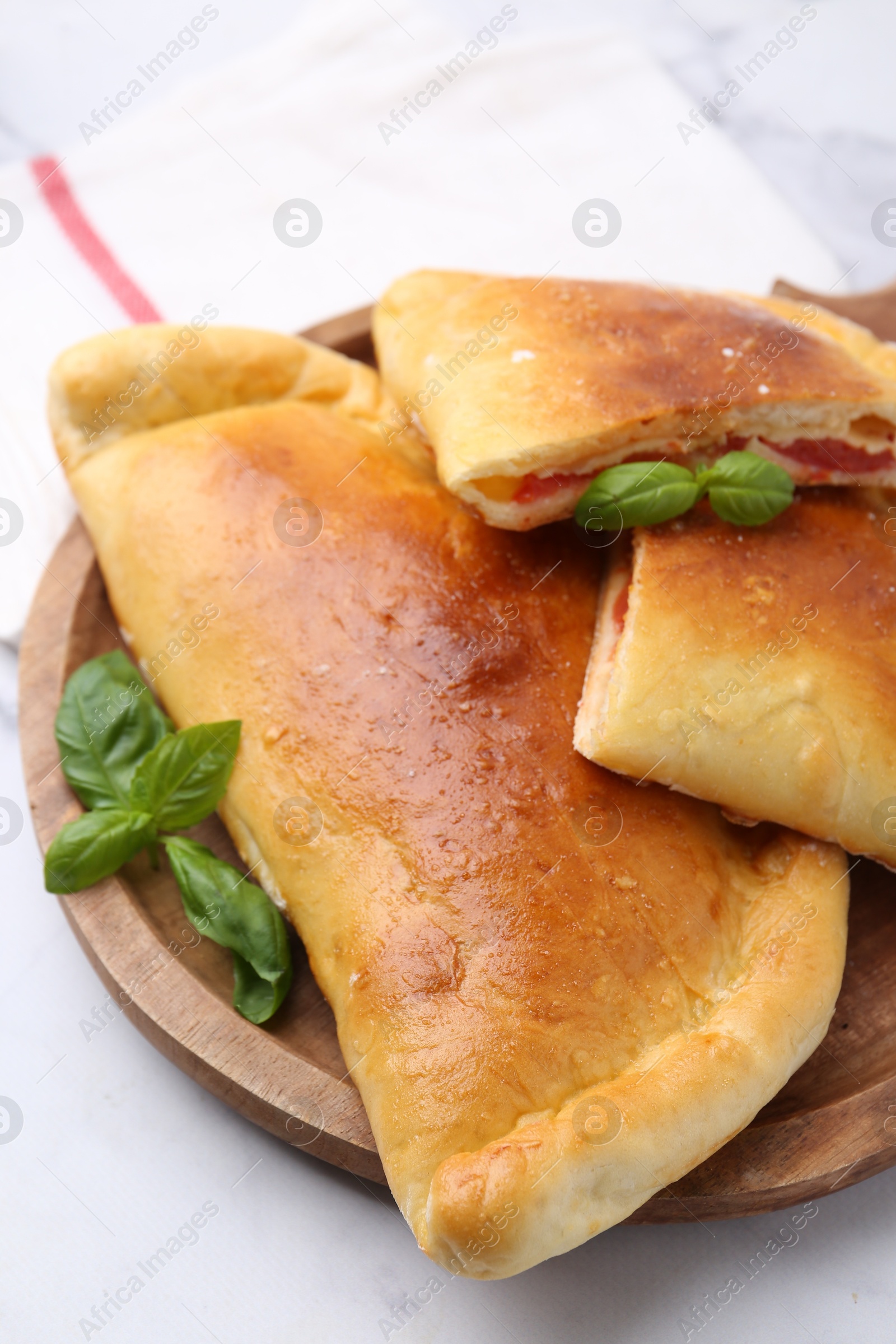 Photo of Tasty vegetarian calzones with tomato, cheese and basil on white table, closeup