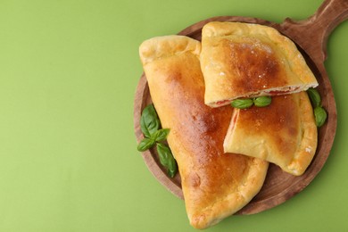 Photo of Tasty vegetarian calzones with tomato, cheese and basil on green background, top view. Space for text