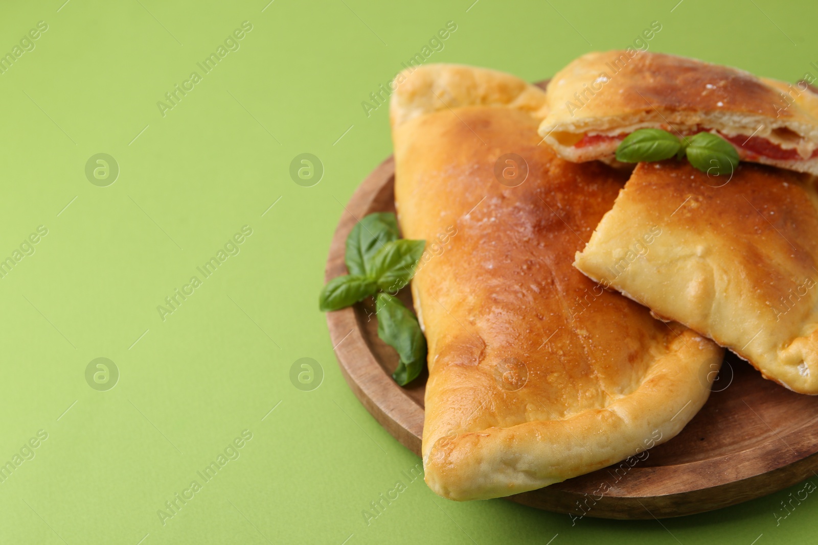 Photo of Tasty vegetarian calzones with tomato, cheese and basil on green background, closeup. Space for text