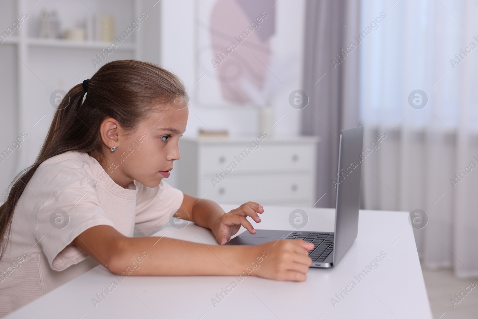 Photo of Girl with incorrect posture using laptop at white desk indoors