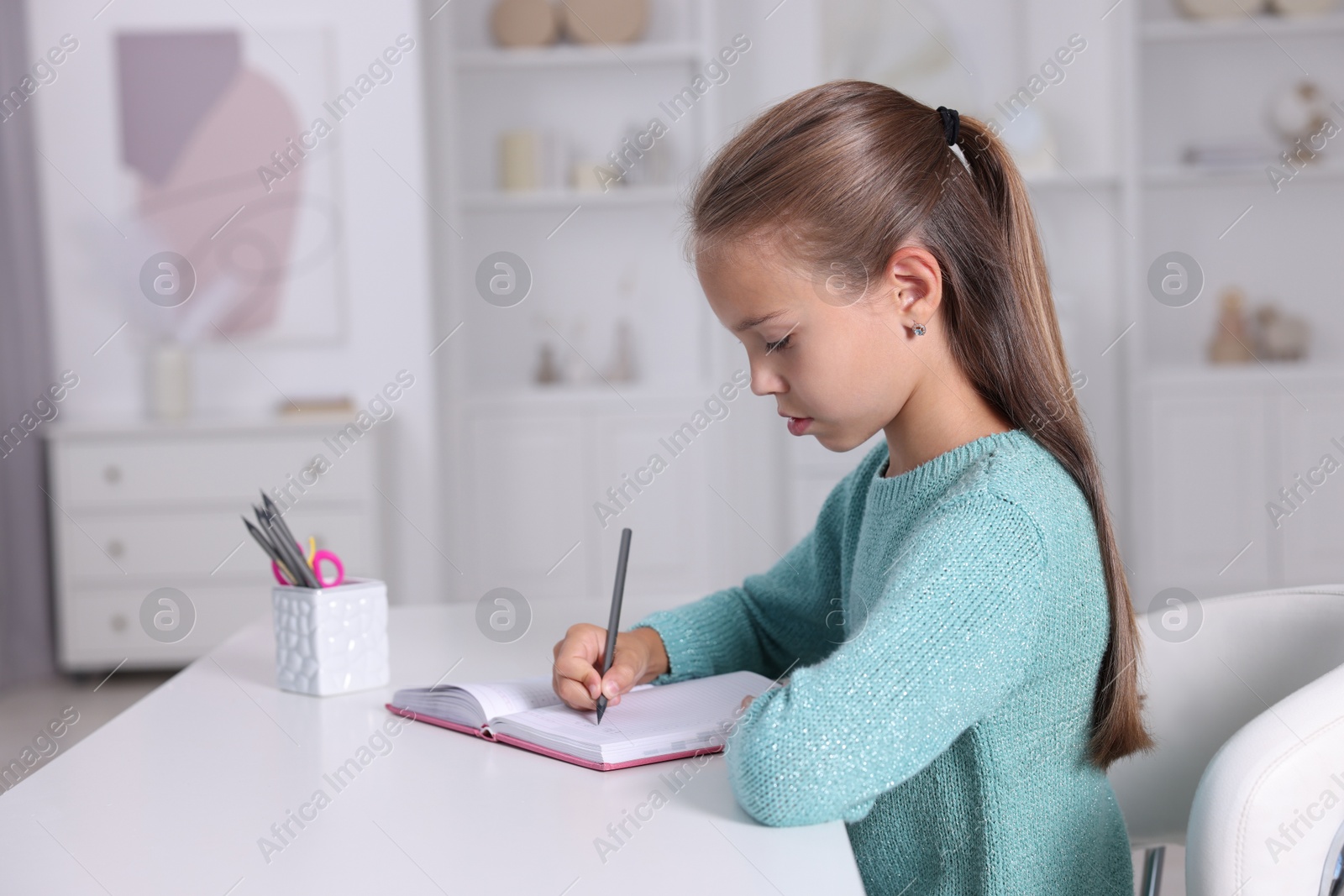 Photo of Girl with correct posture doing homework at white desk indoors