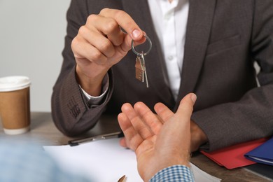 Photo of Real estate agent giving house key to new owner at table, closeup