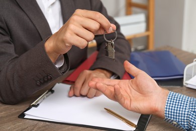 Photo of Real estate agent giving house key to new owner at wooden table, closeup