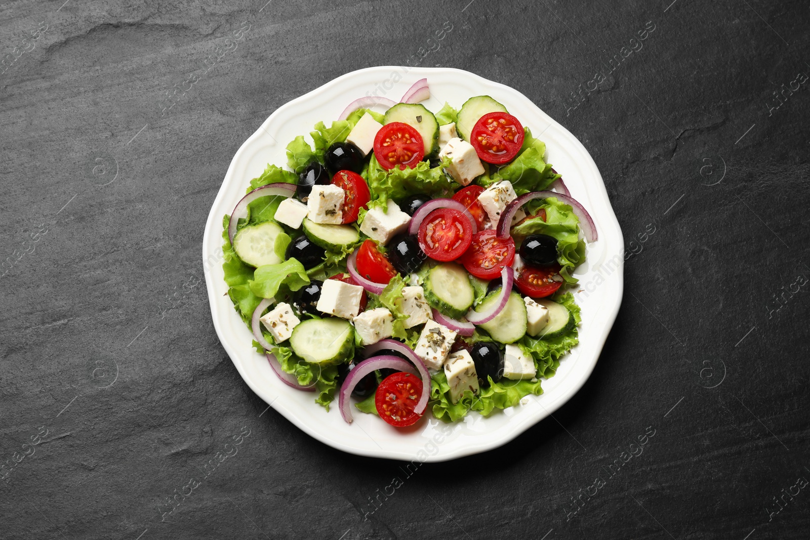 Photo of Delicious salad with feta cheese on dark gray textured table, top view