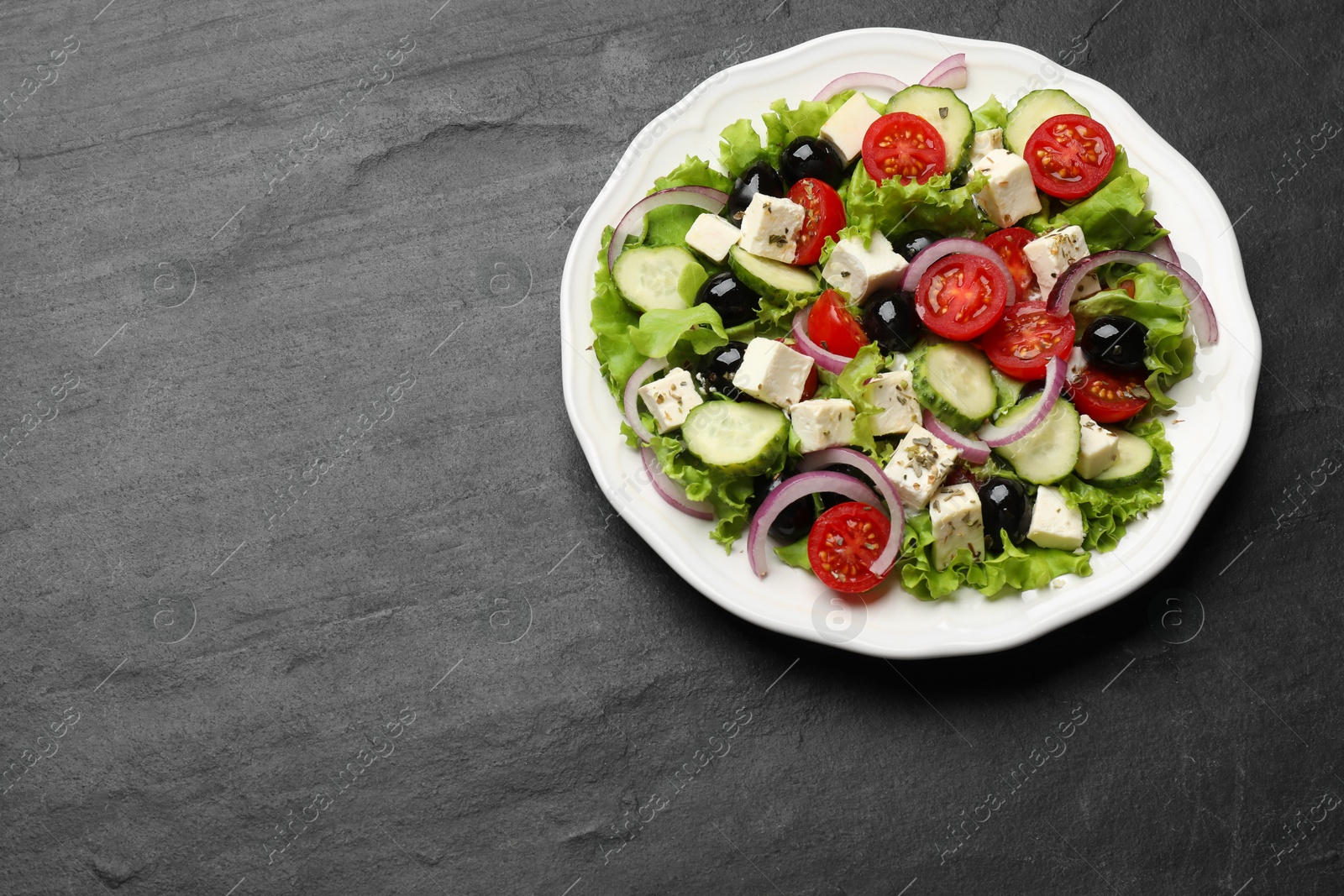 Photo of Delicious salad with feta cheese on dark gray textured table, top view. Space for text