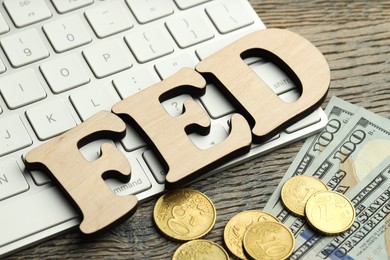 Photo of Word Fed (Federal Reserve System) made with letters, keyboard, dollar banknotes and coins on wooden table, closeup