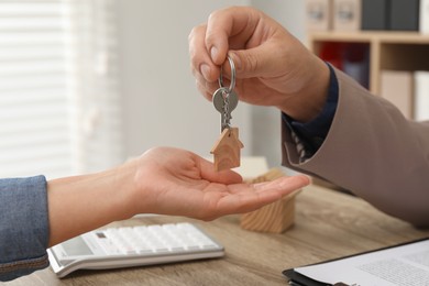 Photo of Real estate agent giving house key to new owner at wooden table, closeup